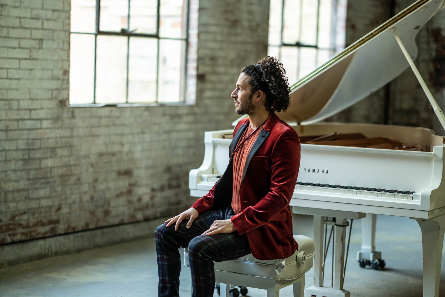 Pianist, Emmet Cohen sitting on a piano bench looking to the left.